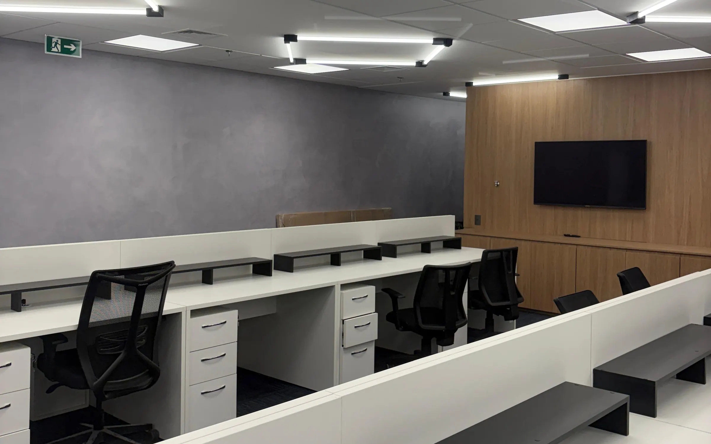 Escritório corporativo entregue, com estações de trabalho brancas, painel de madeira e iluminação linear